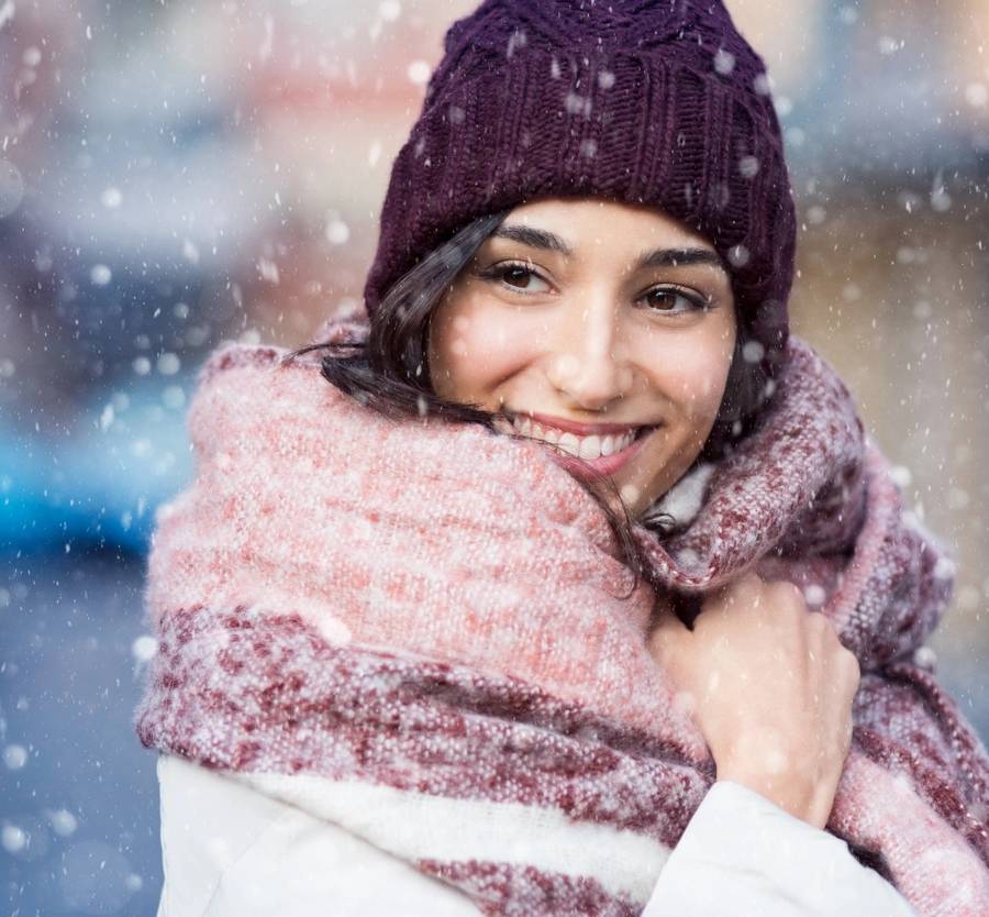 Smiling woman wearing wool bonnet and scarf in a winter cold day. Happy girl in a sweater outdoor in snow. Beautiful smiling woman with hat and scarf outdoor looking away. (Smiling woman wearing wool bonnet and scarf in a winter cold day. Happy girl i